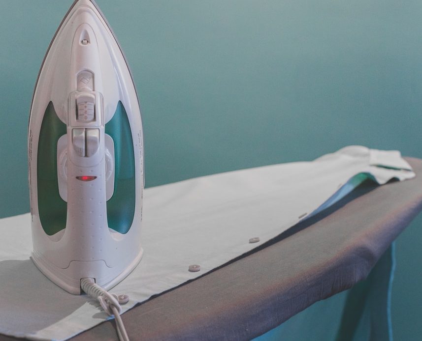 white and teal steam clothes iron plugged on ironing board