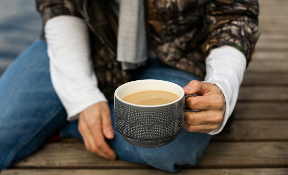 a man sitting on a dock holding a cup of coffee