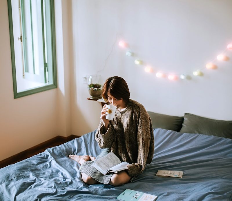 woman in gray sweater sitting on bed