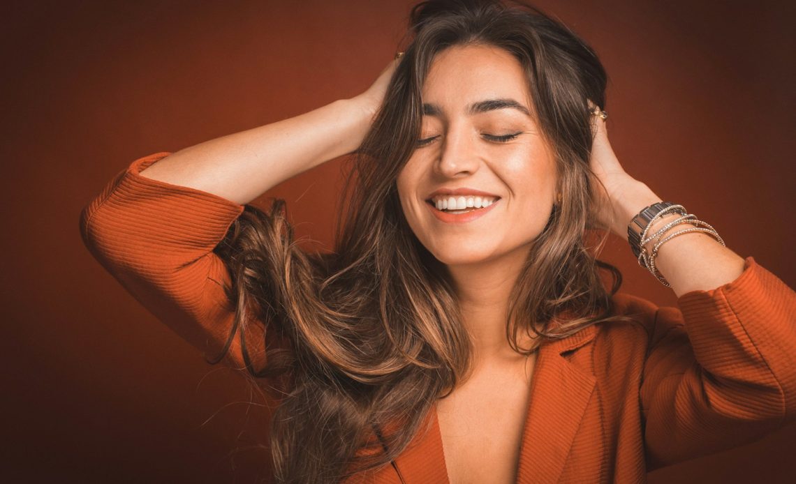 smiling woman in brown top holding hairs