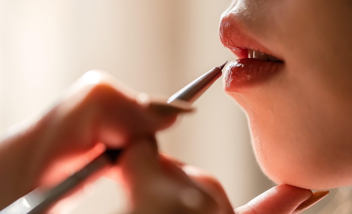 Vrouw die lippenbalsem aanbrengt als onderdeel van een gelaagde lipverzorging routine